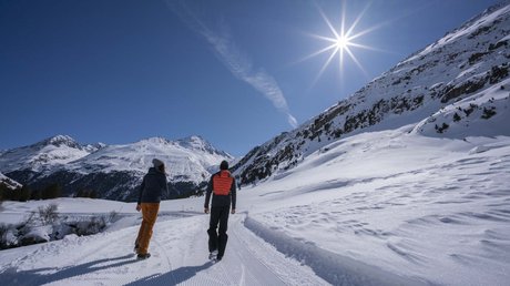 Des impressions de notre hôtel alpin à Vent ! Deux marcheurs sur une route enneigée en montagne sous un soleil éclatant