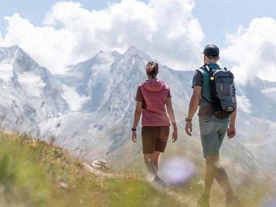 Wandern in den Ötztaler Alpen: von Ihrem Hotel in die Berge Zwei Wanderer gehen auf Pfad vor schneebedeckten Bergen bei bewölktem Himmel