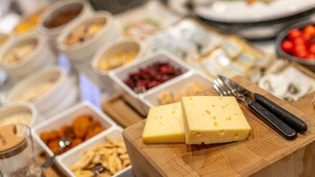 Impressionen aus unserem Natur- und Alpinhotel in Vent Zwei Scheiben Käse auf Holzbrett mit Zutaten und Küchenutensilien im Hintergrund