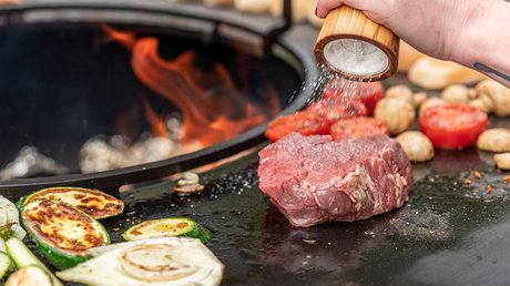 Impressionen aus unserem Natur- und Alpinhotel in Vent Rohe Steakscheibe und Gemüse auf Grill, Hand streut Salz darüber