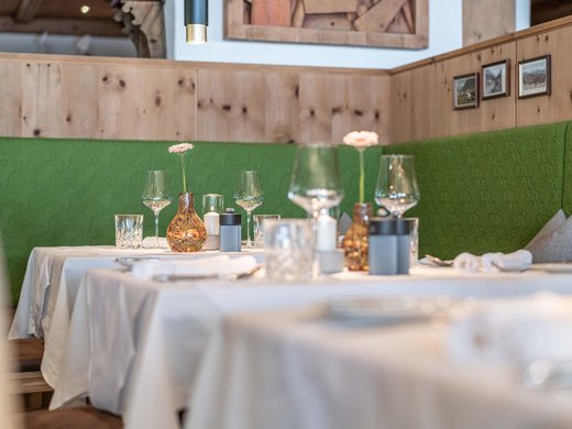 Das Wellnesshotel im Ötztal für Ruhesuchende Gedeckte Tische mit weißen Tüchern und grüner Polsterung in einem Restaurant