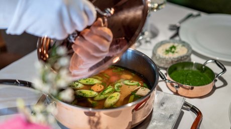 Des impressions de notre hôtel alpin à Vent ! Person soulève le couvercle d'une casserole en cuivre avec bouillon et légumes sur table dressée