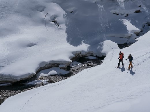 Passez de fantastiques vacances d’hiver au Tyrol. Deux raquetteurs marchent près d'un ruisseau partiellement gelé dans la neige