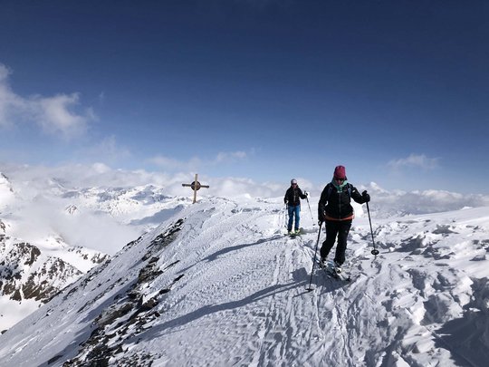Skitouren rund um Vent: direkt von Ihrem Hotel in die Berge Zwei Skifahrer wandern auf schneebedecktem Berggipfel mit Kreuz bei klarem Himmel