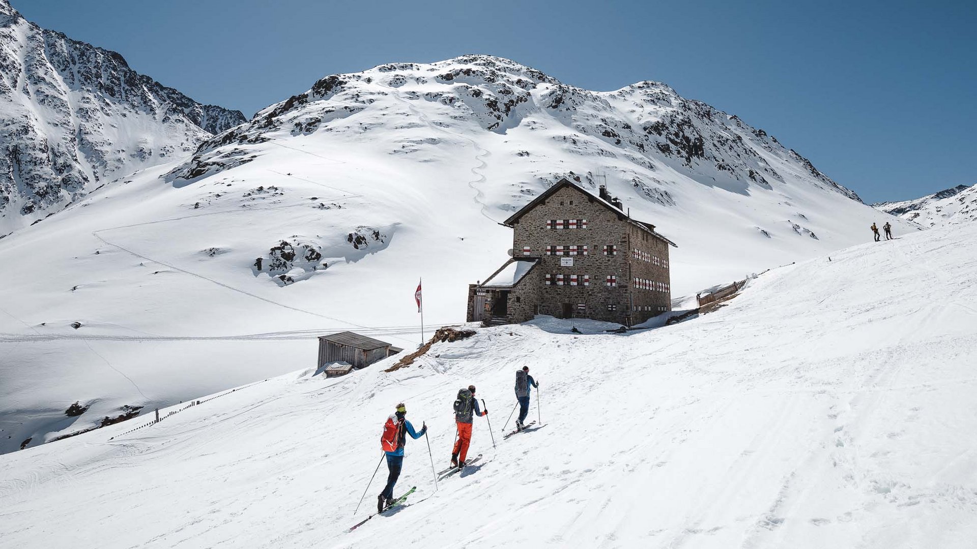Skitouren rund um Vent: direkt von Ihrem Hotel in die Berge Drei Skifahrer vor einer Berghütte in verschneiter Alpenlandschaft bei Sonnenschein
