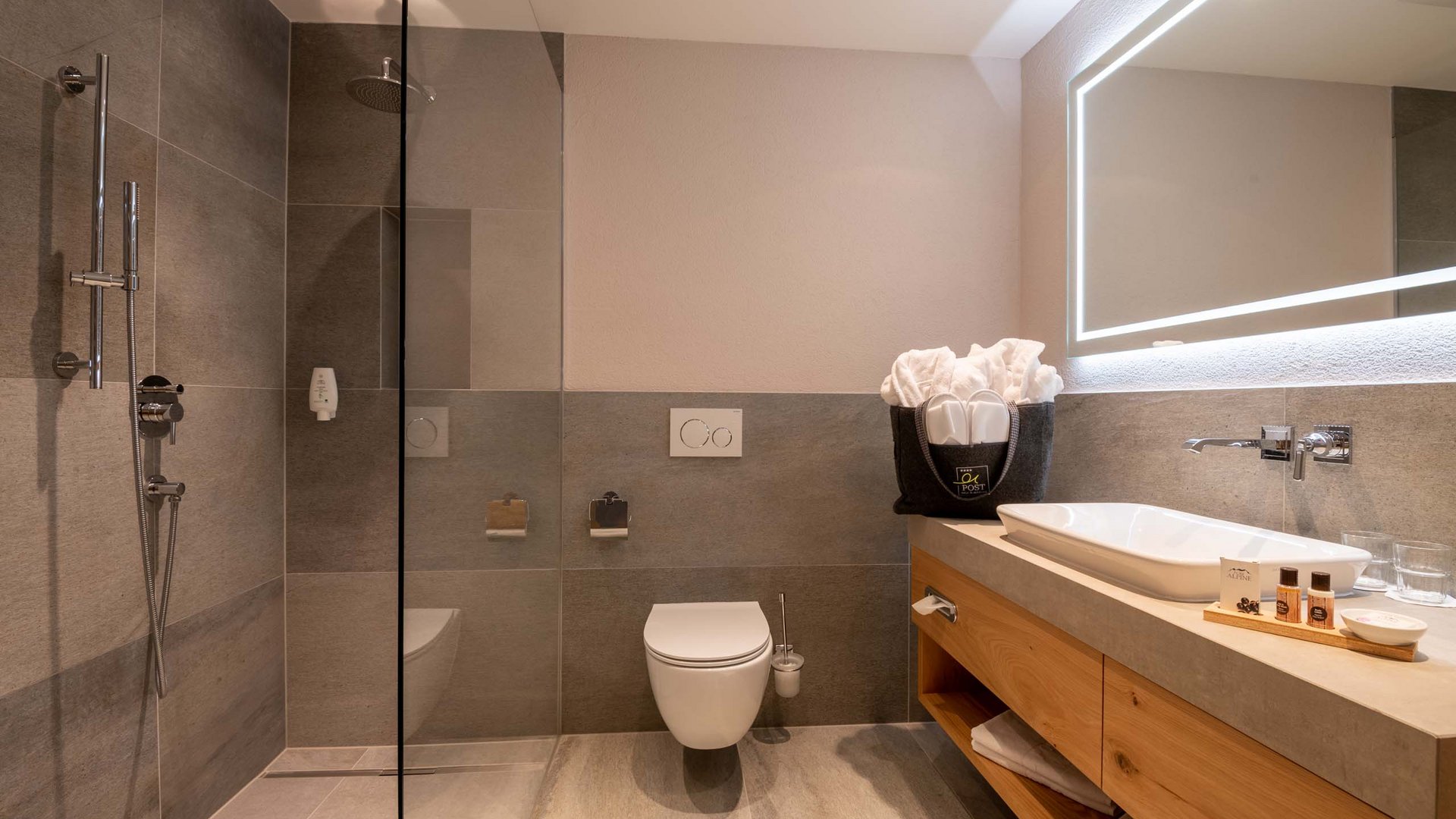 Das Wellnesshotel im Ötztal für Ruhesuchende Modernes Badezimmer mit Dusche, WC und Holzwaschtisch mit beleuchtetem Spiegel