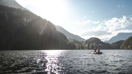 Des impressions de notre hôtel alpin à Vent ! Deux personnes rament sur un lac entouré de montagnes et de forêt au soleil.