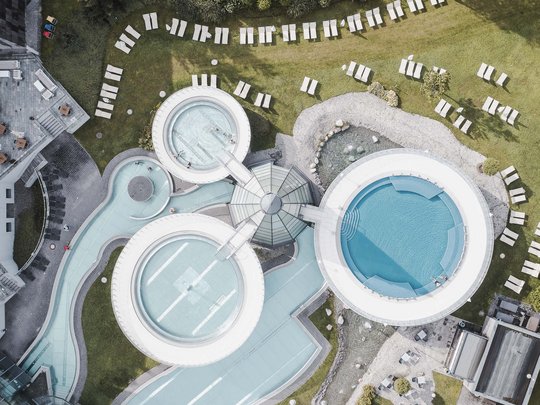 Natur- und Alpinhotel Post: Sehenswürdigkeiten im Ötztal Luftaufnahme eines modernen Schwimmbads mit runden Pools und Liegestühlen auf Rasen