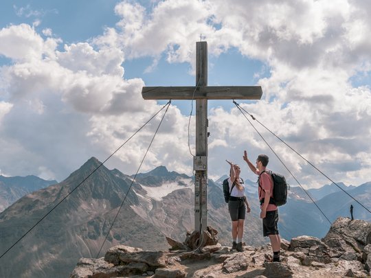 Sur le Similaun et la Wildspitze de notre hôtel à Vent Deux randonneurs font un high-five au sommet d'une montagne à côté d'une grande croix