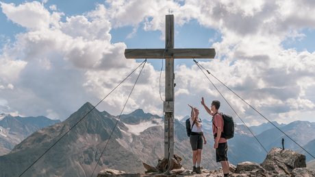 Des impressions de notre hôtel alpin à Vent ! Deux randonneurs font un high-five au sommet d'une montagne à côté d'une grande croix