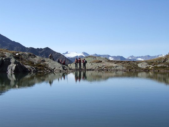 Wandern in den Ötztaler Alpen: von Ihrem Hotel in die Berge Gruppe von Wanderern an einem Bergsee mit schneebedeckten Gipfeln im Hintergrund