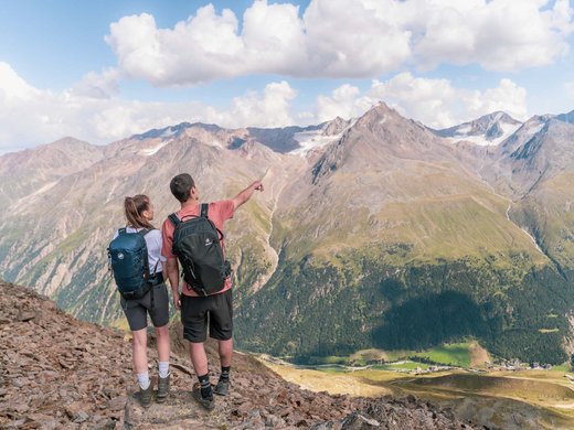 Vacances d’été dans l’Ötztal : un paradis pour les alpinistes Deux randonneurs avec sacs à dos regardent un paysage de montagne avec des nuages