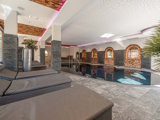 Sauna village & mountain lake: our hotel in Tyrol with pool Modern indoor pool with lounge chairs and wood-tone decor