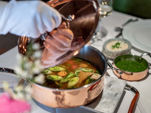 Des plaisirs naturels dans notre restaurant à Vent Person soulève le couvercle d'une casserole en cuivre avec bouillon et légumes sur table dressée