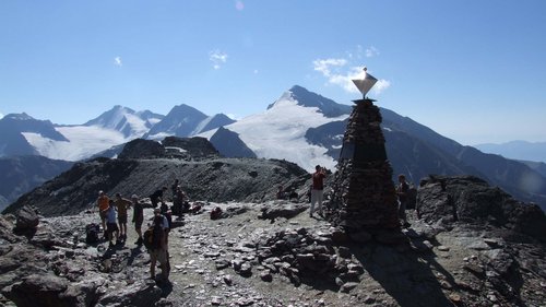 Sehnsuchtsort Vent: unser Hotel im Ötztal Wanderer auf felsigem Berggipfel mit Gletscher und Gipfelzeichen bei sonnigem Himmel