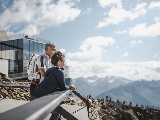 Vacances d’été dans l’Ötztal : un paradis pour les alpinistes Deux randonneurs regardent un paysage montagneux depuis une terrasse moderne